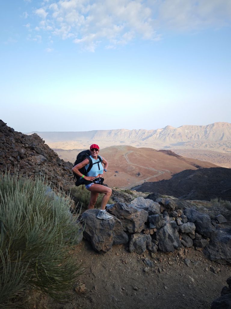 Hiker with a backpack on the rocky switchbacks of the Teide trail, the Las Cañadas caldera behind her