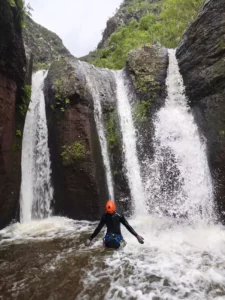 Canyoneer standing in the pool under a triple waterfall in Anaga