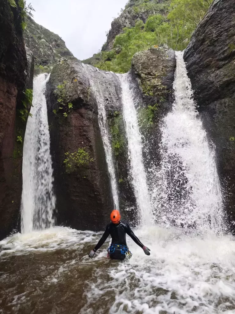 Canyoneer standing in the pool under a triple waterfall in Anaga